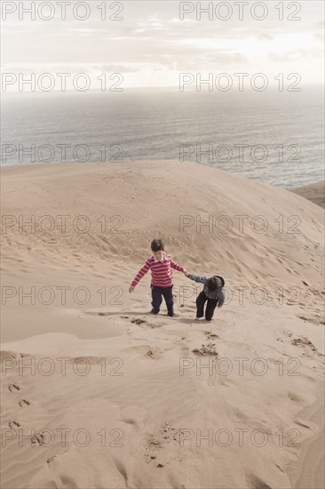 Hispanic brothers climbing on sand dunes on beach