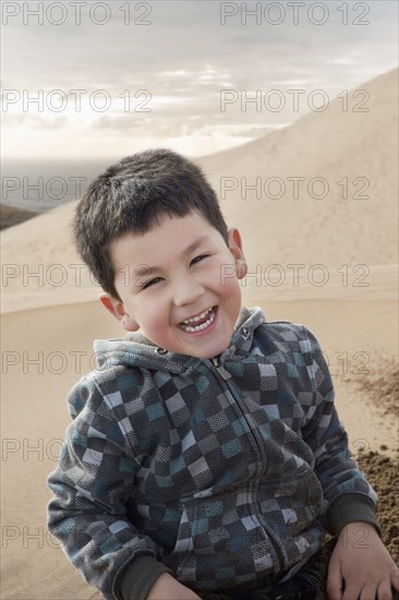 Hispanic boy smiling on sand dune on beach