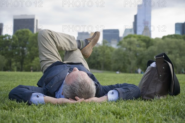 Hispanic businessman laying on grass in urban park