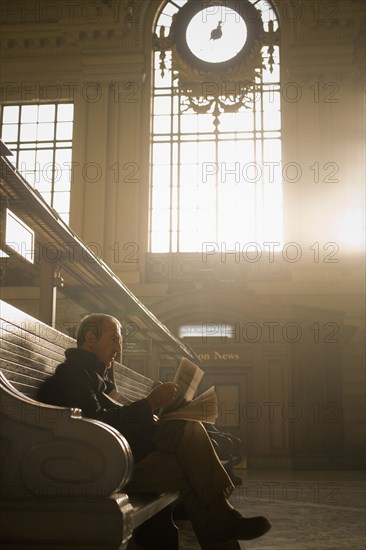 Hispanic man reading newspaper in train station