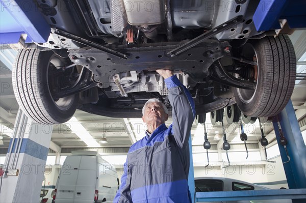 Older Hispanic mechanic repairing car in garage