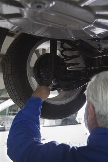 Older Hispanic mechanic repairing car in garage