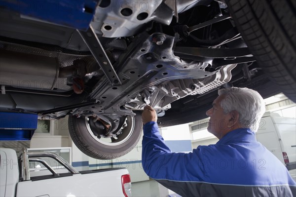 Older Hispanic mechanic repairing car in garage