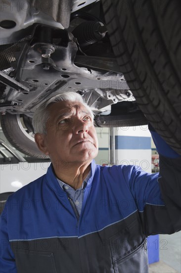 Older Hispanic mechanic repairing car in garage