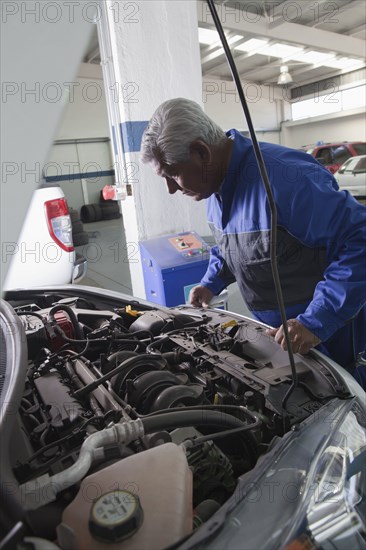 Older Hispanic mechanic examining car in garage