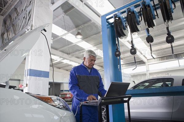 Older Hispanic mechanic using laptop in garage