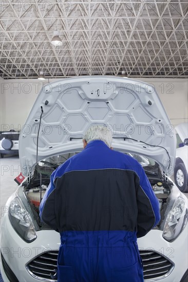 Older Hispanic mechanic repairing car in garage