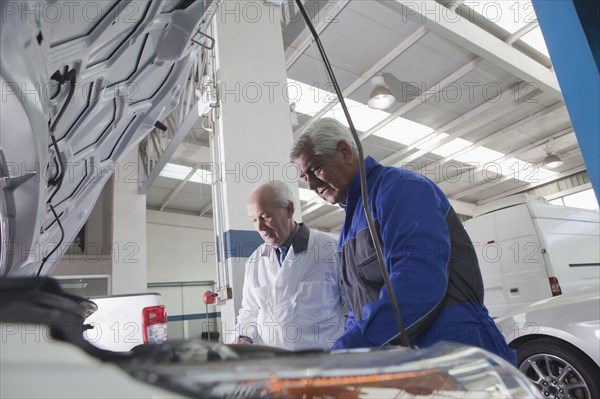 Older Hispanic mechanics repairing car in garage