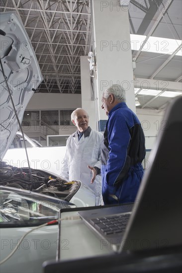 Older Hispanic mechanics discussing car in garage