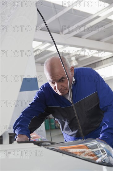 Older Hispanic mechanic repairing car in garage
