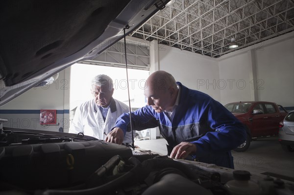 Older Hispanic mechanics repairing car in garage