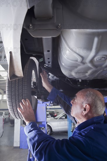 Older Hispanic mechanic repairing car wheel in garage