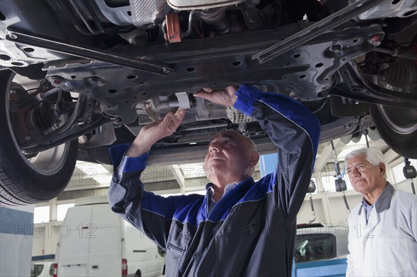 Older Hispanic mechanic repairing car in garage