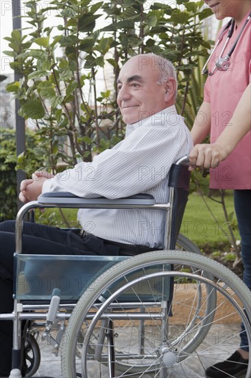 Hispanic nurse pushing patient in wheelchair