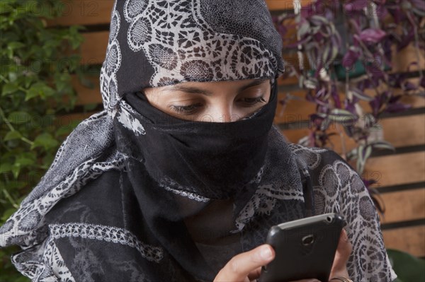 Hispanic woman in headscarf using cell phone