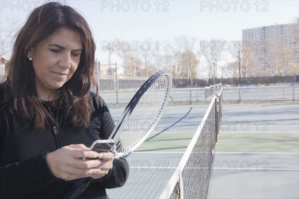 Hispanic woman using cell phone on tennis court