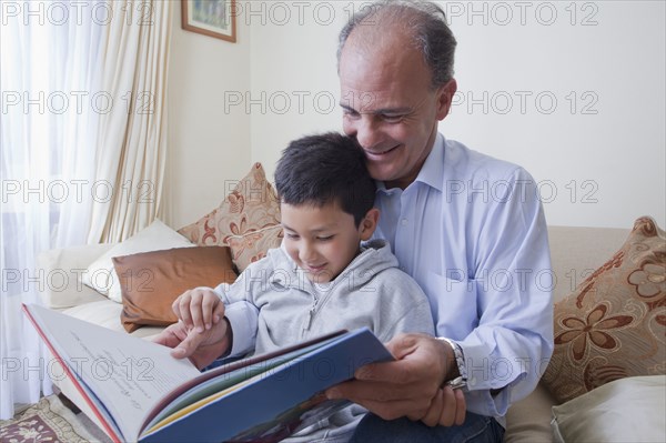 Hispanic father and son reading book on sofa