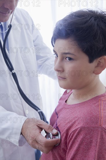 Hispanic doctor listening to chest of boy with stethoscope