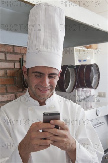 Smiling Hispanic chef texting on cell phone
