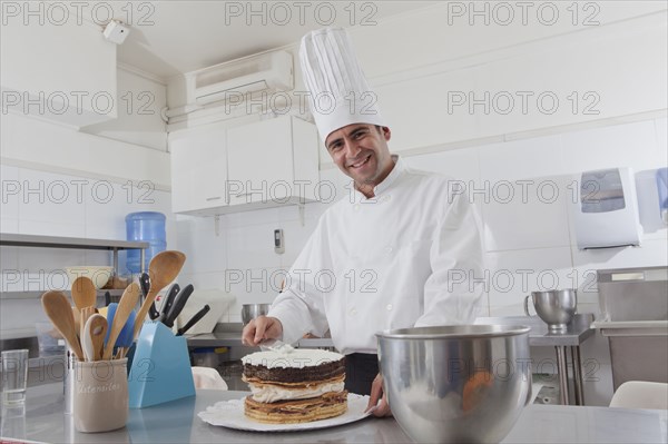 Smiling Hispanic chef spreading icing on cake