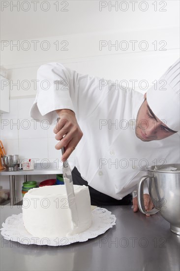 Hispanic chef spreading icing on side of cake