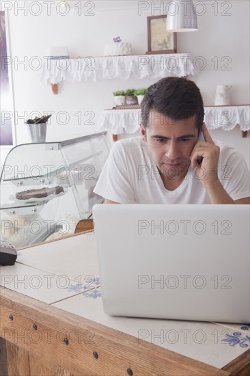 Hispanic baker using laptop and cell phone