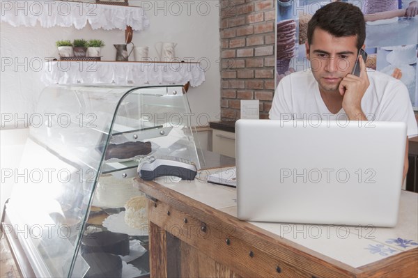 Hispanic baker using laptop and cell phone