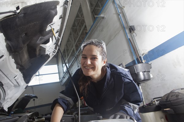 Smiling Hispanic mechanic repairing car engine