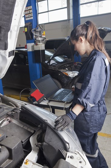 Hispanic mechanic diagnosing car engine with laptop