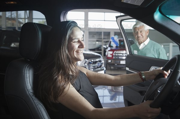 Hispanic woman sitting in car in dealership showroom