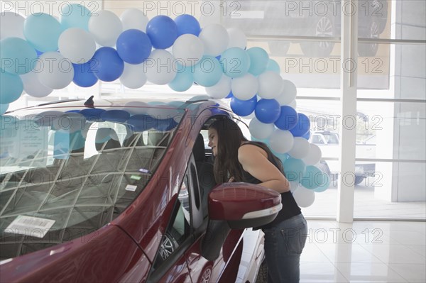 Hispanic woman examining car in dealership showroom