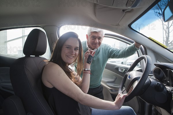 Hispanic woman sitting in new car showing key