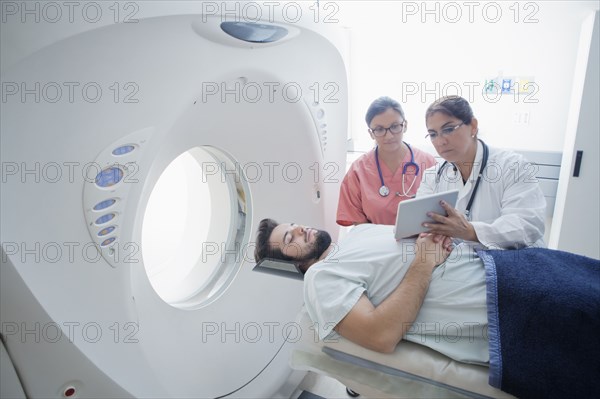 Hispanic doctor and nurse showing digital tablet to patient at scanner