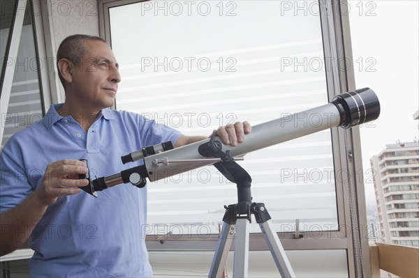 Hispanic man holding telescope near window