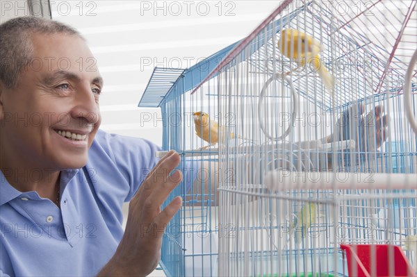 Smiling Hispanic man admiring birds in birdcage