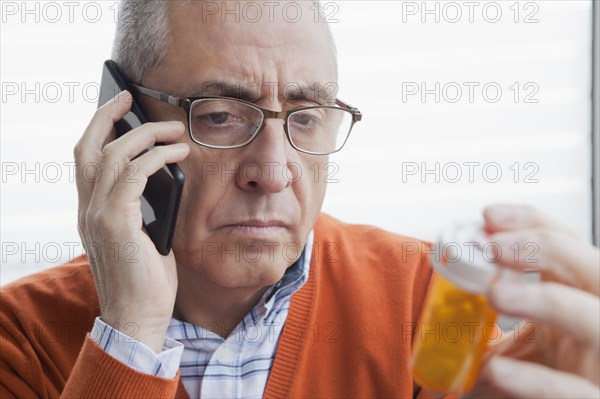 Serious Hispanic man talking on cell phone holding prescription bottle