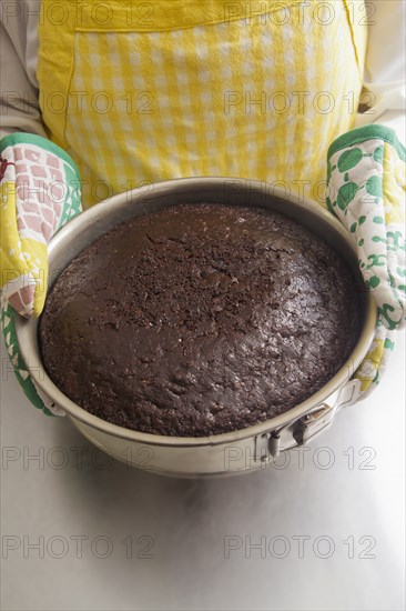 Hispanic woman holding cake in pan with oven mitts