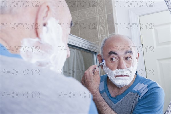 Reflection of Hispanic man shaving face in mirror