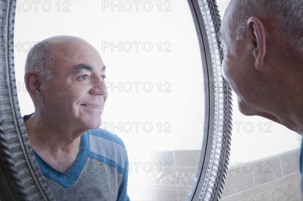 Reflection of smiling Hispanic man in bathroom mirror