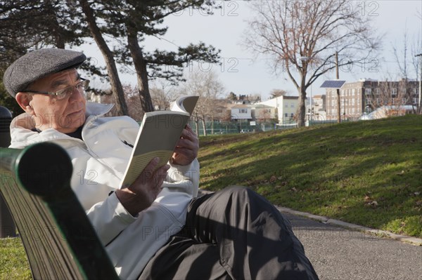 Hispanic man sitting on park bench reading book