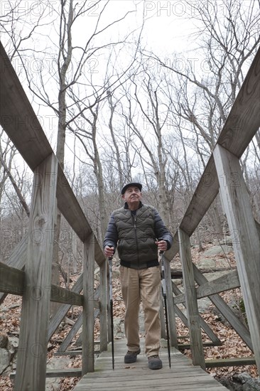 Hispanic man walking on footbridge using walking sticks