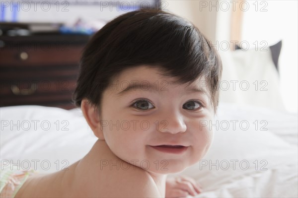 Portrait of smiling Hispanic baby boy laying on bed