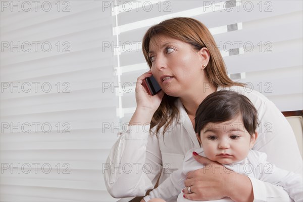 Hispanic mother holding baby boy and talking on cell phone