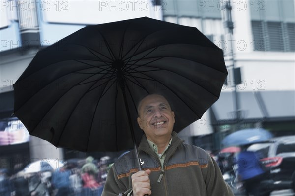 Smiling Hispanic man holding umbrella in city