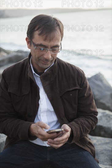 Mixed Race man texting on cell phone at beach