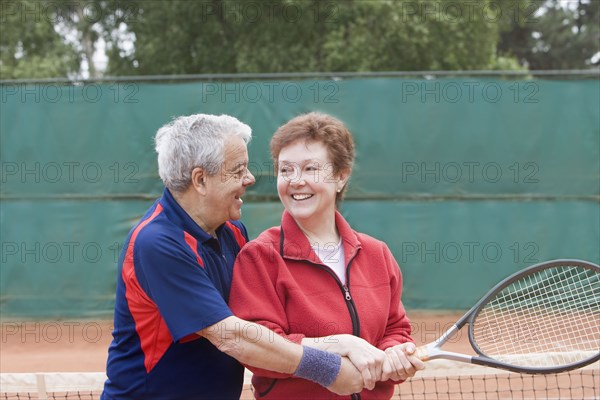 Senior Hispanic man teaching wife to play tennis