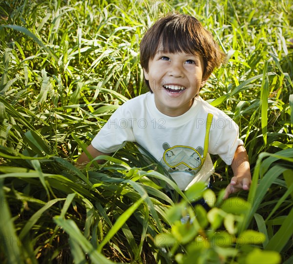 Grinning mixed race boy sitting in long grass