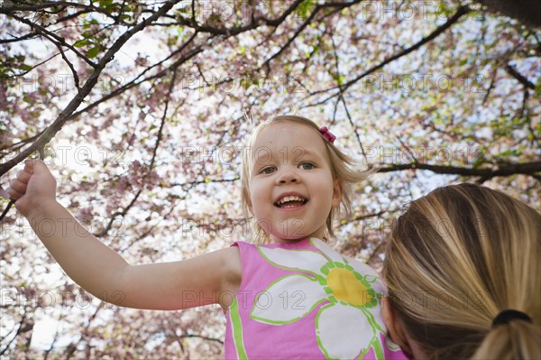 Mother lifting daughter under spring flowers