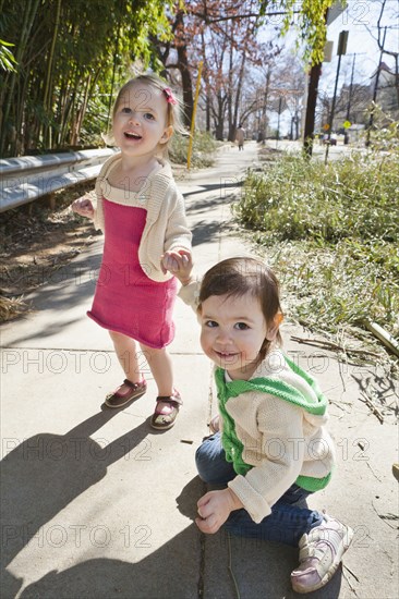 Caucasian girls holding hands on sidewalk