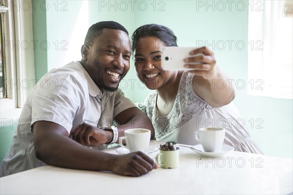 Smiling couple taking cell phone selfie at table